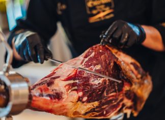 Don Esteban Gourmet Debuts Its First Boutique Location at Radisson Blu Aruba; A New Culinary Experience Showcasing Authentic Spanish Artisanship A person cutting meat with a knife Description automatically generated